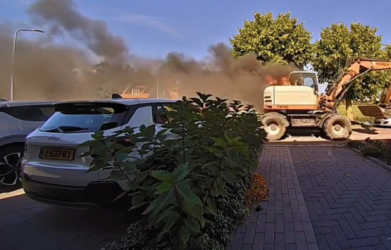 Brandende graafmachine rijdt door straat na plotselinge brand